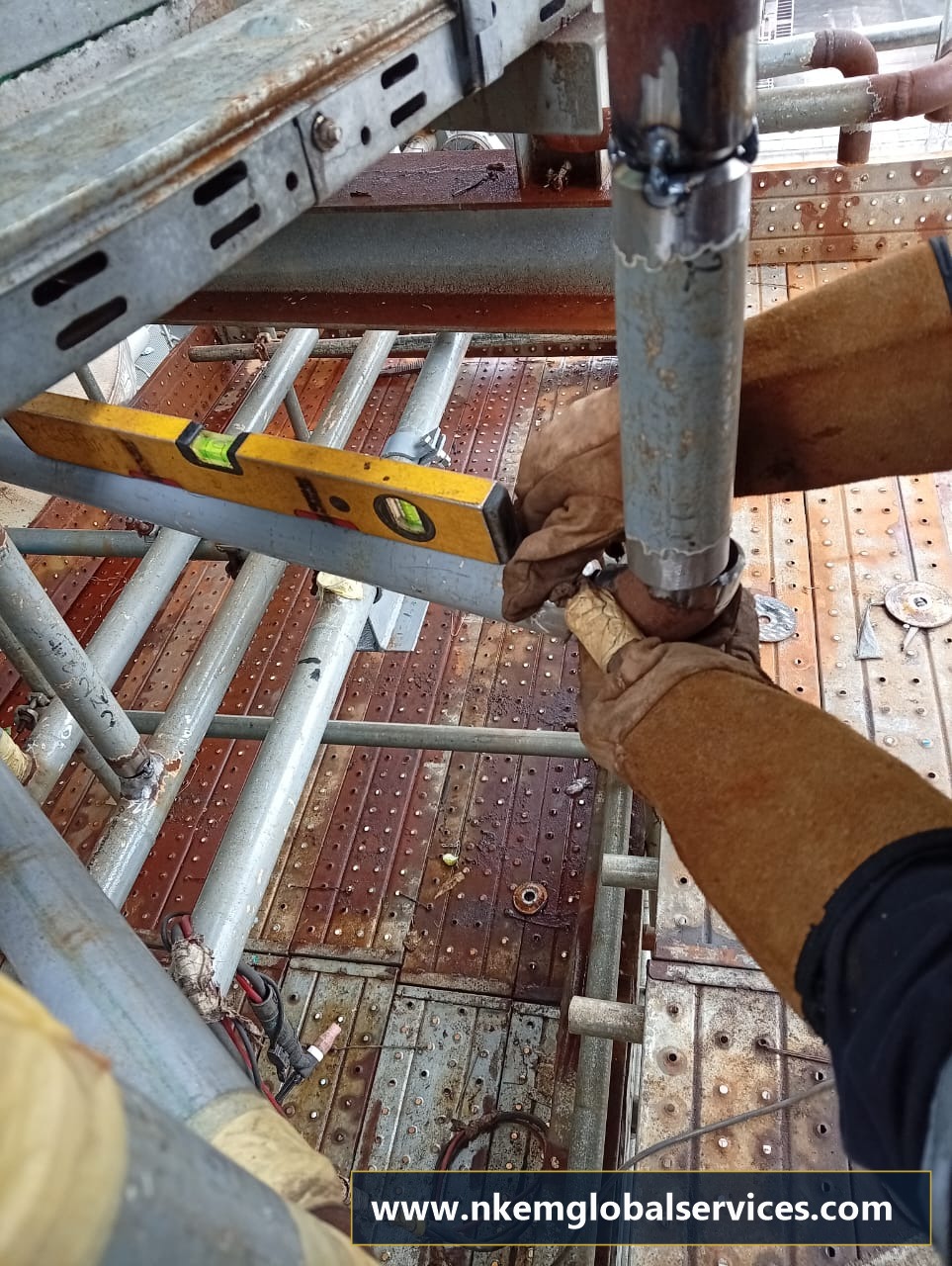 Pipe fitter checking branch elbow alignment with spirit level on staging
